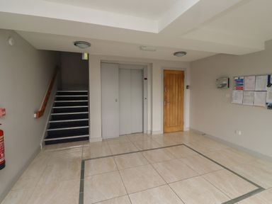 A lobby area with a staircase an elevator a wooden door and a bulletin board at Assisi Apartment in Alnmouth