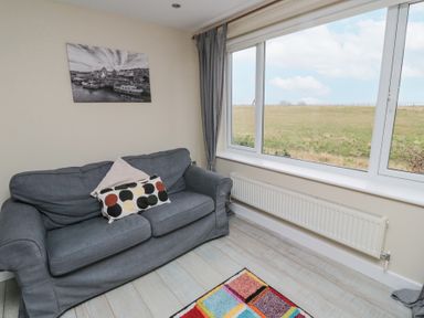 A sitting area with a grey sofa and cushions next to a large window showing a field at Beach View in Seahouses