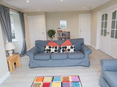 A living room with a blue sofa two doors a bookshelf a potted plant a lamp and a colorful rug at Beach View in Seahouses