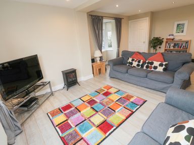 A living room with blue sofas and a colorful rug at Beach View in Seahouses