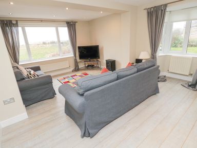A living room with two gray sofas a TV on a stand a small heater a table lamp and large windows at Beach View in Seahouses