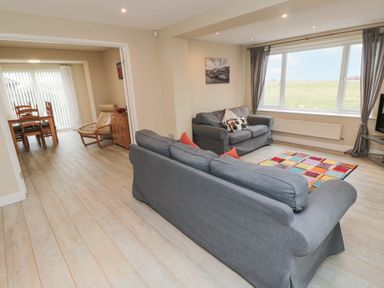 A living room with two gray sofas a colorful rug and a dining area with a wooden table and chairs at Beach View in Seahouses
