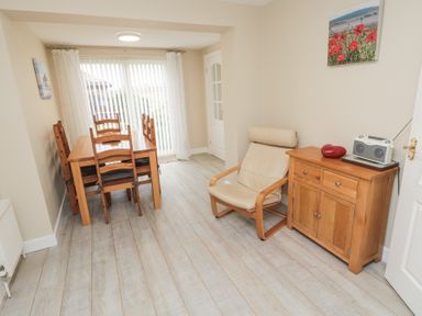 A dining area with a wooden table and chairs next to sliding glass doors a beige armchair and a wooden cabinet with a radio and decoration on top at Beach View in Seahouses