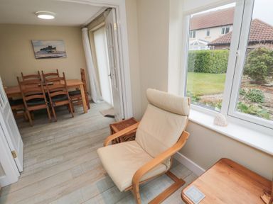 A room with a beige chair next to a window and a wooden dining table with chairs in the background at Beach View in Seahouses