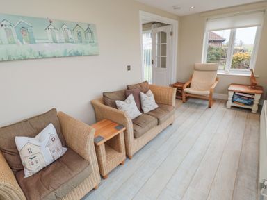 A sitting room with wicker armchairs a wooden side table a wooden armchair and a window at Beach View in Seahouses