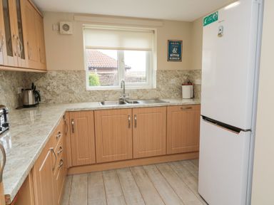 A kitchen with wooden cabinets a double sink a white refrigerator and kitchen appliances on the countertop at Beach View in Seahouses
