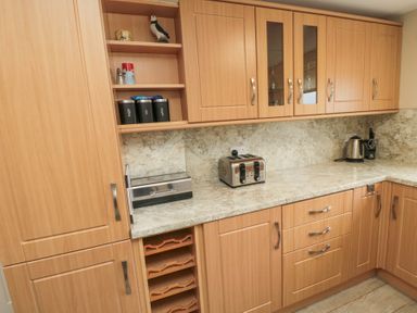 A kitchen with wooden cabinets a toaster a kettle a bread box and shelves with canisters at Beach View in Seahouses
