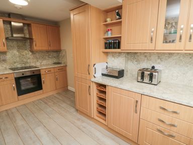 A kitchen with wooden cabinets a built in oven toaster and bread box at Beach View in Seahouses