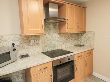 A kitchen with wooden cabinets a glass stovetop an oven a microwave and tiled flooring at Beach View in Seahouses