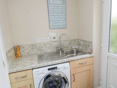 A utility room with a washing machine under a countertop with a sink and a faucet at Beach View in Seahouses