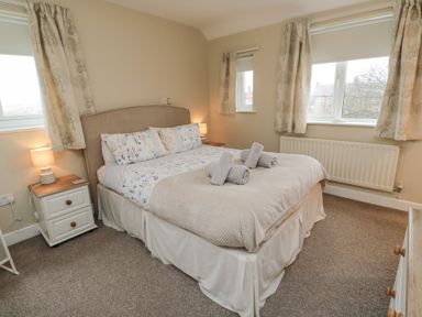 A bedroom with a double bed side tables lamps and windows with curtains at Beach View in Seahouses