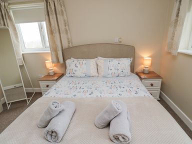 A bedroom with a double bed with patterned bedding two bedside tables with lamps rolled towels on the bed and a standing mirror near a window at Beach View in Seahouses