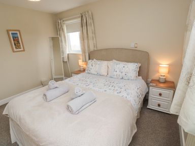 A bedroom with a double bed two bedside tables with lamps and a standing mirror at Beach View in Seahouses