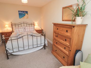A bedroom with a metal bed frame two bedside tables with lamps a wooden chest of drawers with a mirror and plant on top and a painting on the wall at Beach View in Seahouses