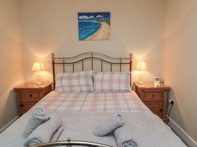 A bedroom with a metal bed frame two bedside tables with lamps a painting above the bed at Beach View in Seahouses