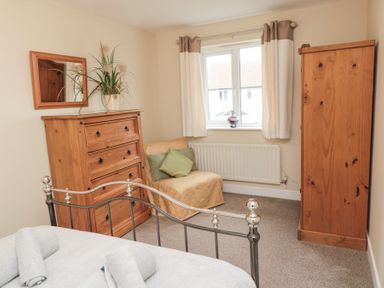 A bedroom with a bed a wooden chest of drawers a chair with cushions a wardrobe and a window at Beach View in Seahouses