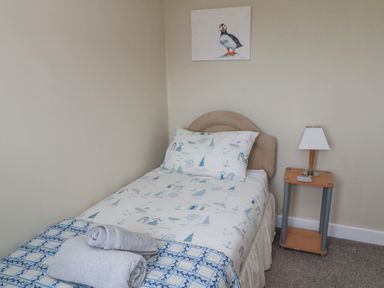 A bedroom with a single bed a bedside table with a lamp and a painting of a bird on the wall at Beach View in Seahouses