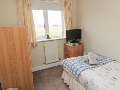 A bedroom with a single bed a small wooden cabinet a television on the cabinet and a window with curtains at Beach View in Seahouses