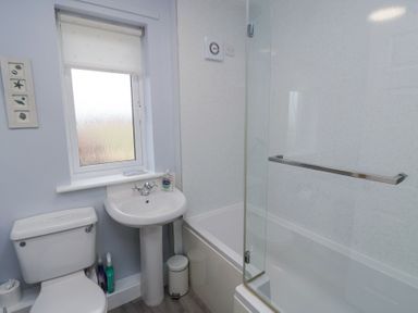 A bathroom with a toilet sink and bathtub with glass screen at Beach View in Seahouses