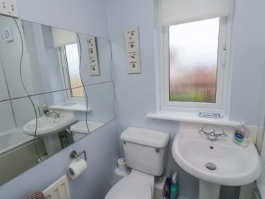 A bathroom with a toilet sink mirror window and toiletries at Beach View in Seahouses