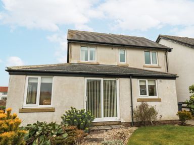 The rear view of a two story house with a garden and sliding glass doors at Beach View in Seahouses