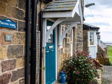 A stone house exterior with a blue door numbered 5 and bushes beside it at Begonia House in Alnmouth