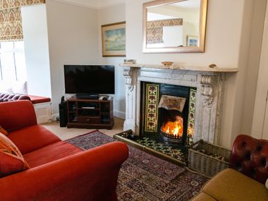 A living room with a fireplace a television on a stand and red sofas at Begonia House in Alnmouth