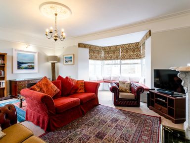 A living room with red sofa chair tv and patterned blinds at Begonia House in Alnmouth