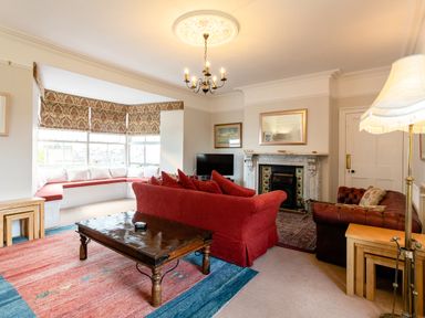 A living room with a red sofa a wooden coffee table a fireplace and a corner window seat at Begonia House in Alnmouth