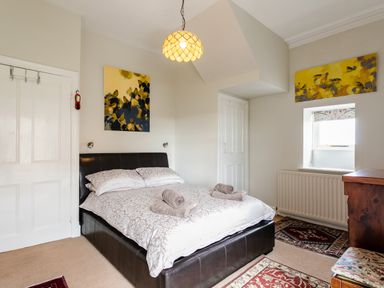 A bedroom with a double bed with towels on the bed and paintings on the walls at Begonia House in Alnmouth