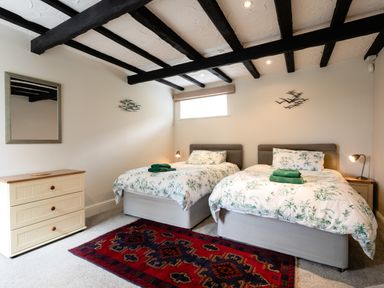 A bedroom with two single beds a chest of drawers a mirror and a rug at Begonia House in Alnmouth