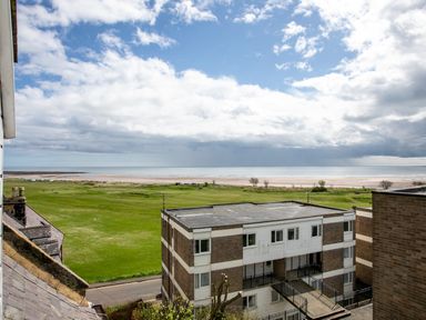 View of grassy area and beach beyond with residential buildings in foreground at Begonia House in Alnmouth