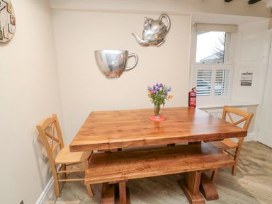 A wooden dining table with a bench and two chairs a vase with flowers on the table and a window with shutters in a dining area at Begonia House in Alnmouth