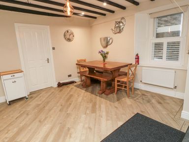 A dining area with a wooden table bench and chairs a clock and teapot wall decorations at Begonia House in Alnmouth