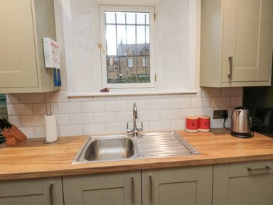 A kitchen sink with a faucet below a window with cabinets on both sides at Begonia House in Alnmouth