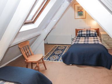An attic bedroom with two single beds a wooden chair a framed picture and a skylight window at Begonia House in Alnmouth