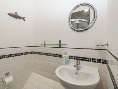 A bathroom corner with a white sink a round mirror a soap dispenser a toilet paper holder and a fish wall decoration at Begonia House in Alnmouth