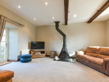 A living room with a brown sofa a wood stove a flat screen tv on a wooden stand and two blue cushions on the floor at Budle Granary in Bamburgh