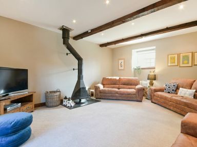 A living room with two brown sofas a black wood stove a television on a wooden stand and ceiling beams at Budle Granary in Bamburgh