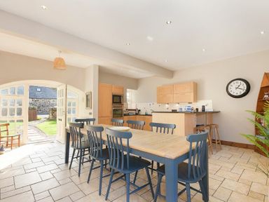 A kitchen with a wooden dining table and blue chairs and an open door showing a garden at Budle Granary Bamburgh