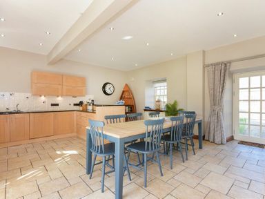 A kitchen with light wood cabinets a wooden dining table with blue chairs tiled floor and a glass door at Budle Granary in Bamburgh