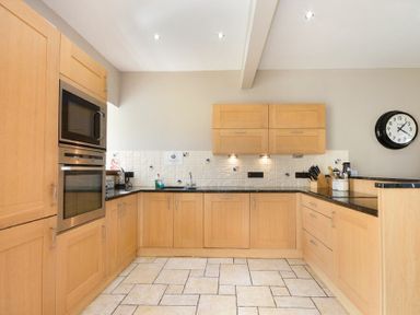 A kitchen with light wood cabinets built in microwave and oven tiled floor and wall clock at Budle Granary in Bamburgh