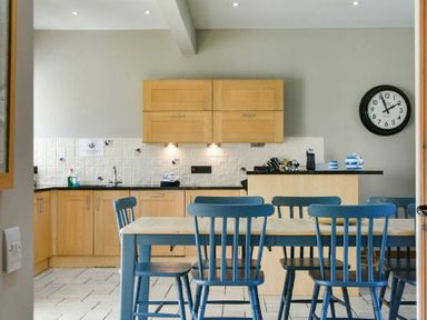 A kitchen with wooden cabinets blue chairs and a dining table at Budle Granary Bamburgh