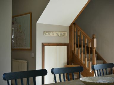 A dining area with dark wooden chairs a staircase with wooden railing and a sign that reads Gone to the Beach at Budle Granary in Bamburgh