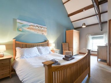 A bedroom with a wooden bed frame and side tables with lamps a wardrobe a chair and a window at Budle Granary in Bamburgh