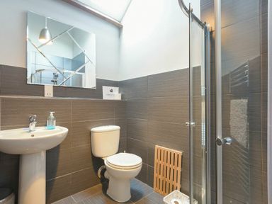 A bathroom with a pedestal sink a toilet a mirror and a glass shower enclosure at Budle Granary in Bamburgh