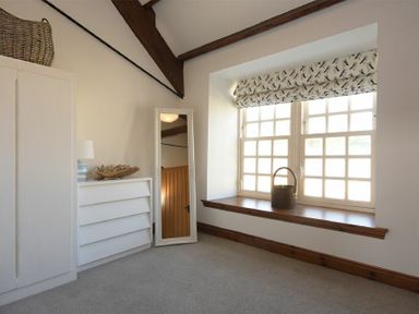 A room with a white dresser a standing mirror a large window with patterned blinds and a basket on the windowsill at Budle Granary in Bamburgh