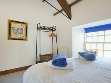 A bedroom with a bed with folded towels a window with a blue blind a clothing rack with hangers and a wicker basket at Budle Granary in Bamburgh