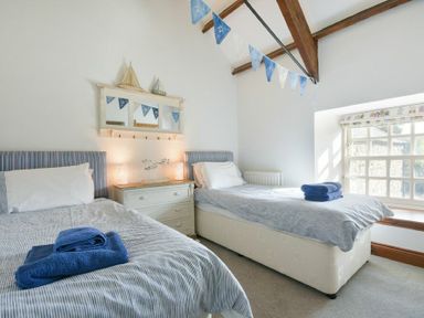 A bedroom with two single beds a dresser between them and a large window at Budle Granary in Bamburgh