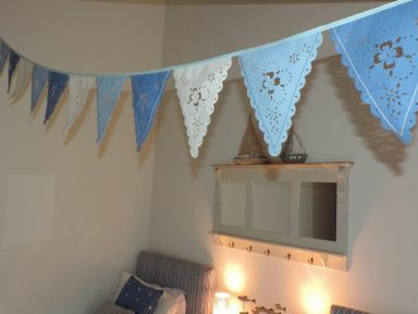 Bedroom corner with blue and white bunting hanging above twin beds with striped headboards and blue pillows and a wall shelf with decorative boats at Budle Granary Bamburgh